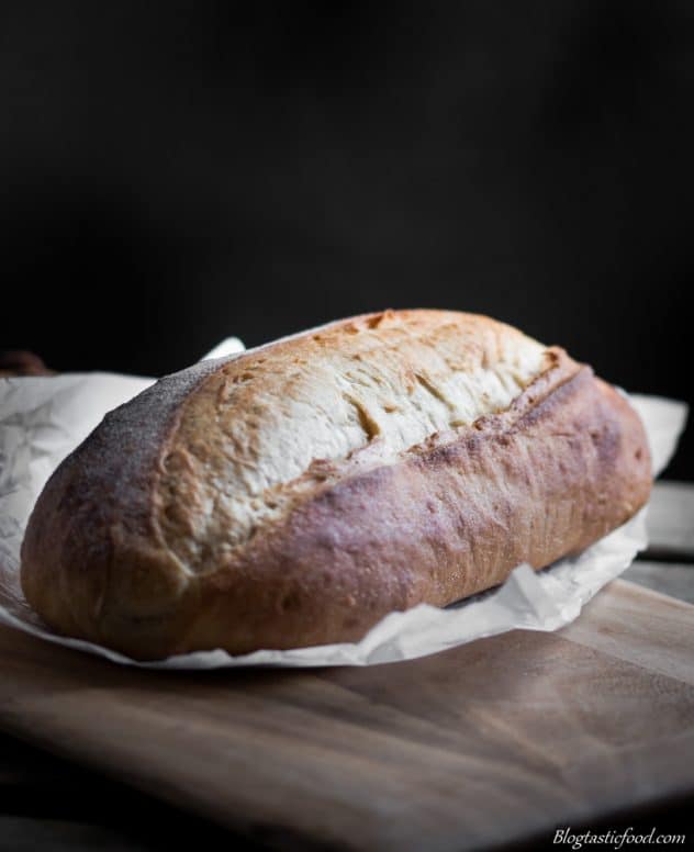 A dark, moody photo of sour dough bread on a piece of baking paper.