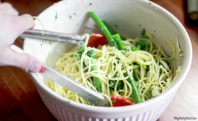 A photo of some mixing spaghetti and broccolini through carbonara sauce.