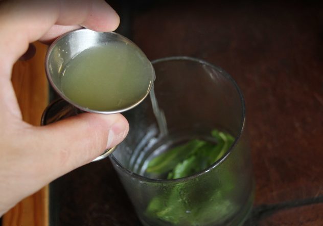 Someone adding lime juice to a chilled glass with fresh mint in it. 