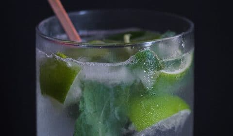 A close up photo of someone stirring a mojito in a chilled glass.
