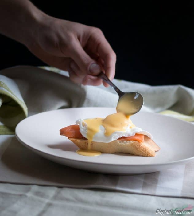 A photo of someone spooning hollandaise sauce on top of a poached egg.