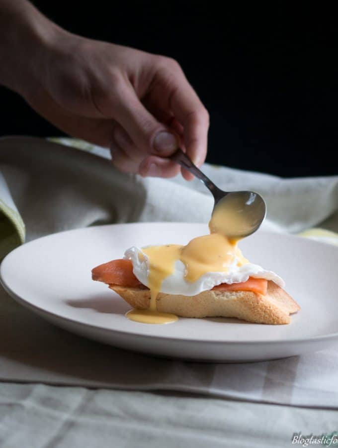 A photo of someone spooning hollandaise sauce on top of a poached egg.
