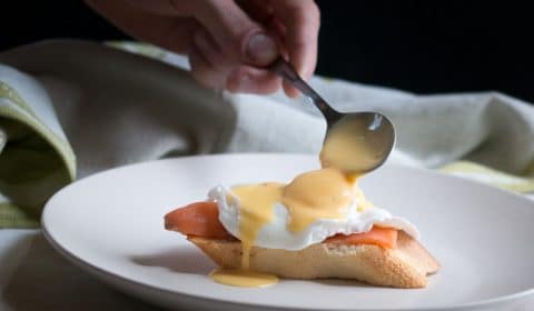 Holloandaise sauce getting spooned over a poached egg and smoked salmon.