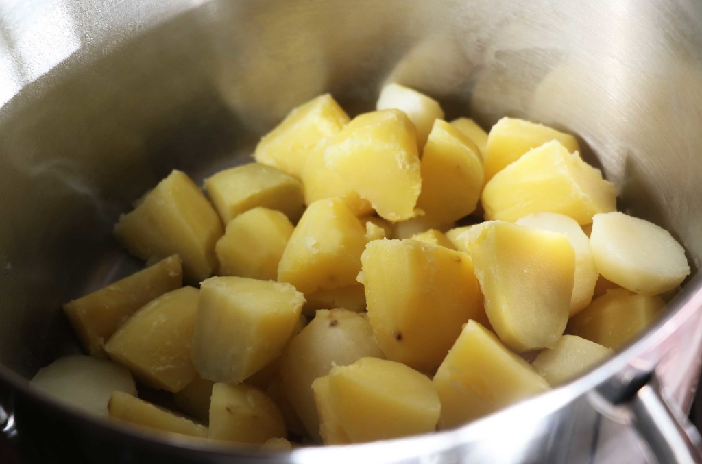 Boiled, diced potatoes in a stainless steel pot. 