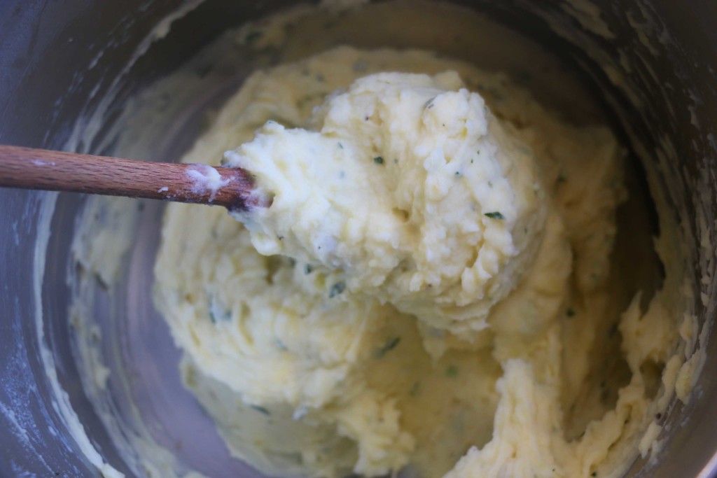 a overhead photo of a wooden spoon stirring mashed potato in a pot. 