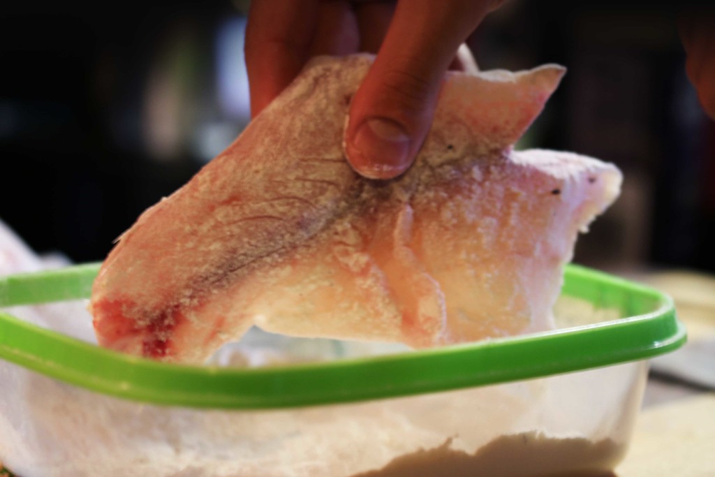 A fillet of raw snapper being dusted in plain flour. 