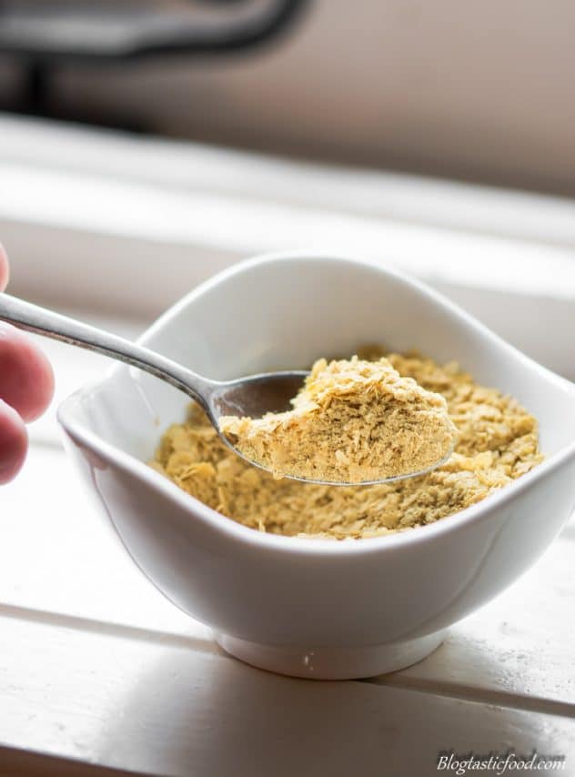 This is a photo of a silver spoon scooping some nutritional yeast out of a ramekin. 