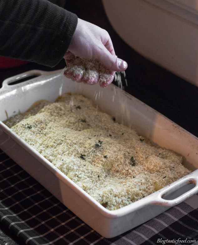 A photo of someone sprinkling some panko breadcrumbs over creamy scalloped potatoes. 