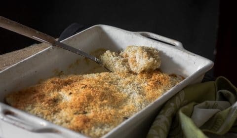 Vegan potato gratin with a golden browned panko breadcrumb topping served in a baking tray with a large spoon scooping out some of the potato.
