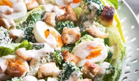 A close up photo of broccoli Caesar salad with spiced Caesar dressing on a nice big white platter.