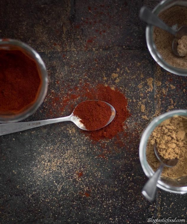 An over head photo of ground cumin, ground coriander and paprika in jars and small spoons.