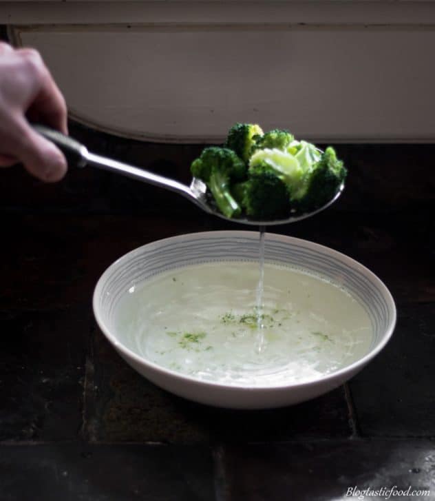 Someone using a slotted spoon to take broccoli out a bowl of water.