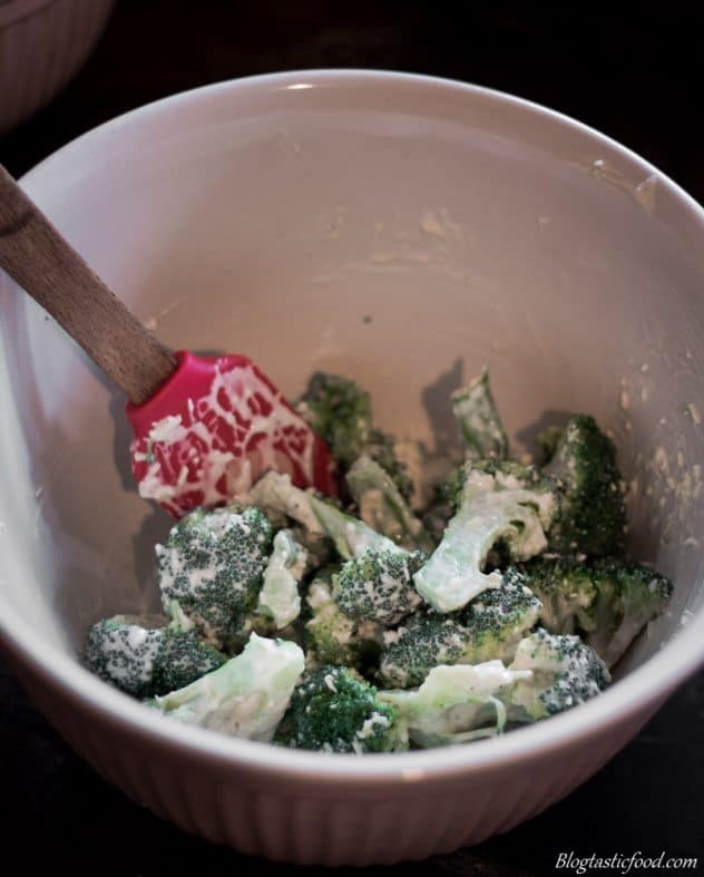 Broccoli being tossed through spiced Caesar dressing in a bowl.