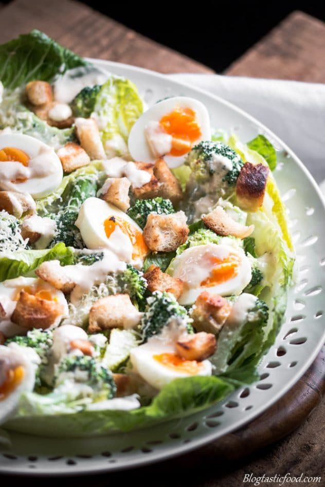 A close up photo of broccoli Caesar salad on a white platter.