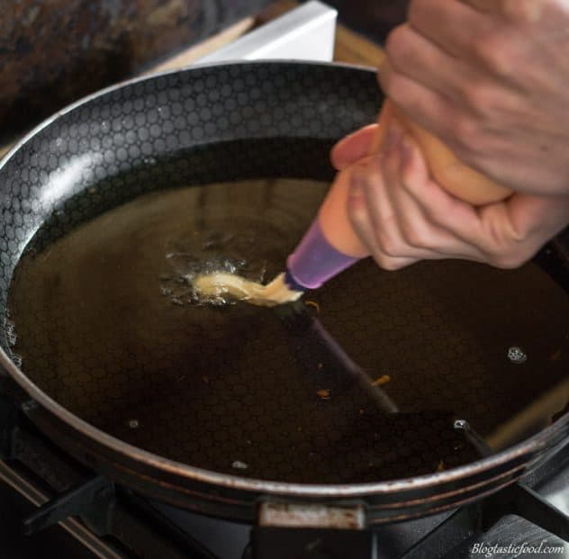 A photo of choux paste being piped into hot oil.
