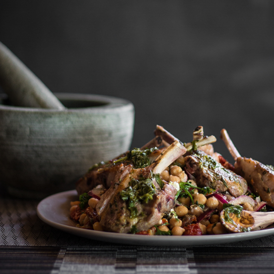 A photo of lamb cutlets served on chickpea salad, with a pestle mortar in the background.