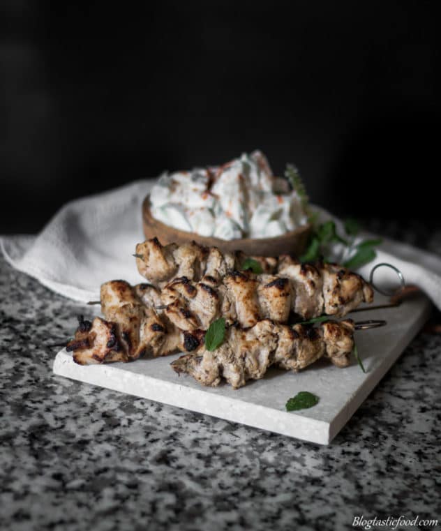 Cucumber raita and chicken tikka skewers served garnished with parsley with a white cloth in the background. 