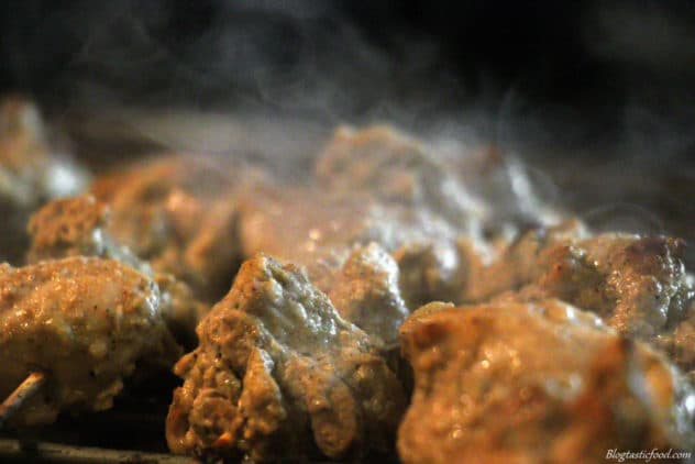 A close up photo of chicken tikka skewers with smoke rising off of it. 
