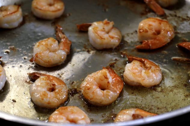 A close up photo of peeled prawns being pan fried in olive oil.