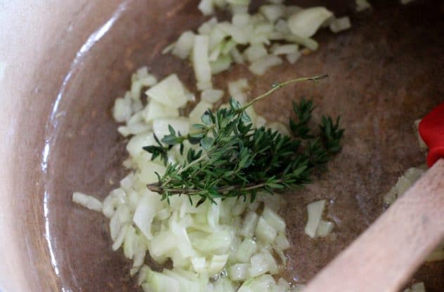 A photo of onions frying of in a pot with a bundle of fresh thyme.