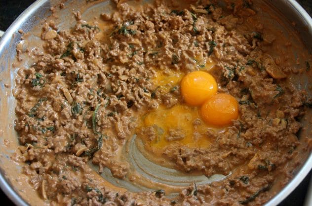Egg yolk being added to a creamy beef mixture.