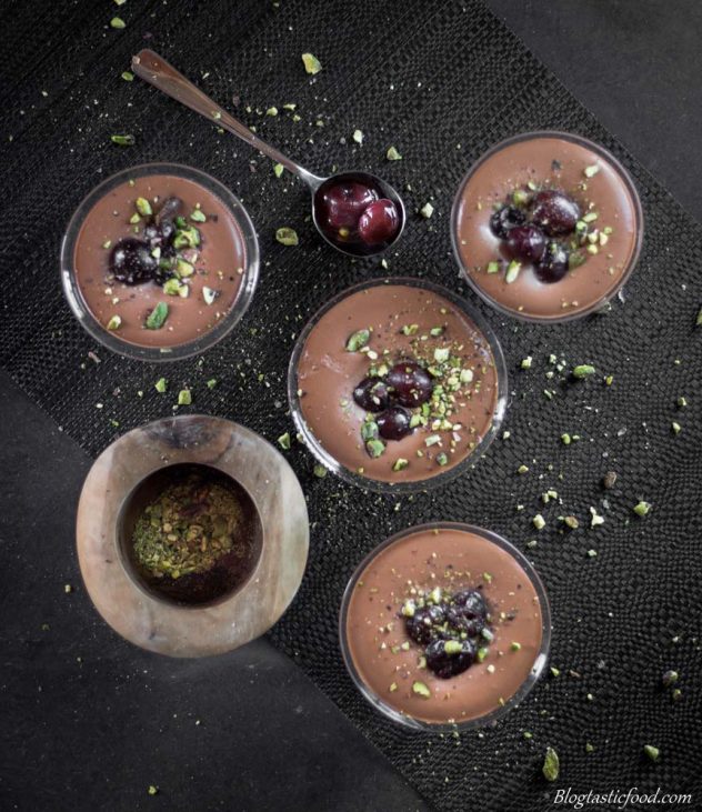 A overhead photo of chocolate mousse in glasses with cherries and crushed pistachios on top.