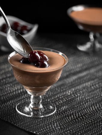 Alcohol Soaked Cherries being spooned over a glass filled with mint chocolate mousse.
