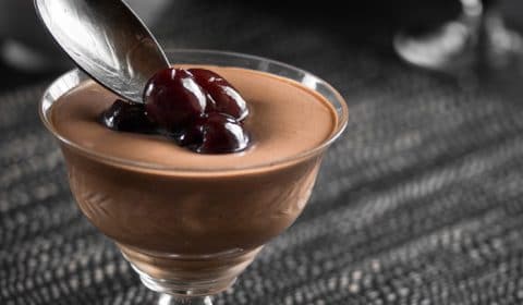 Alcohol Soaked Cherries being spooned over a glass filled with mint chocolate mousse.