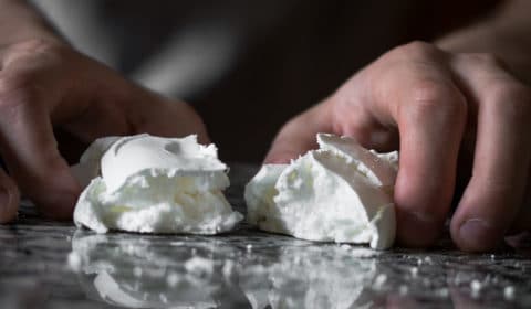 Some breaking a meringue in half on a table.