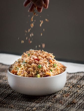 Some crispy fried shallots getting sprinkled over a nice big bowl of vegetable fried rice.