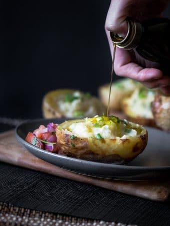 A dark moody photo of someone drizzling extra virgin olive oil over twice baked potatoes served with fresh salsa.