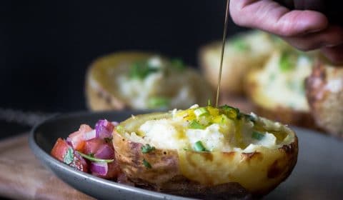 A dark moody photo of someone drizzling extra virgin olive oil over twice baked potatoes served with fresh salsa.