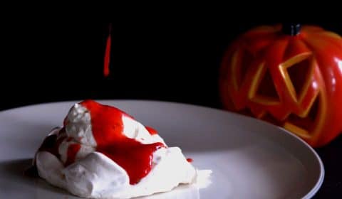 A photo of strawberry coulis being spooned over meringue on a plate.