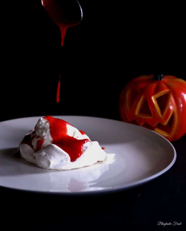 A photo of strawberry coulis being spooned over meringue on a plate. 