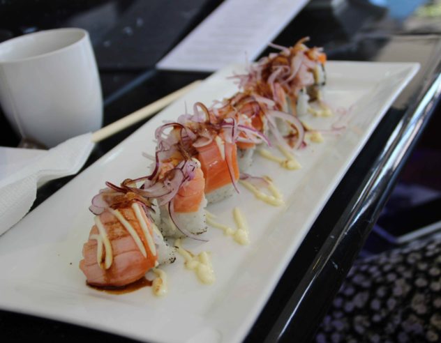 A platter of seared salmon sushi nigiri topped with thinly sliced red onions.