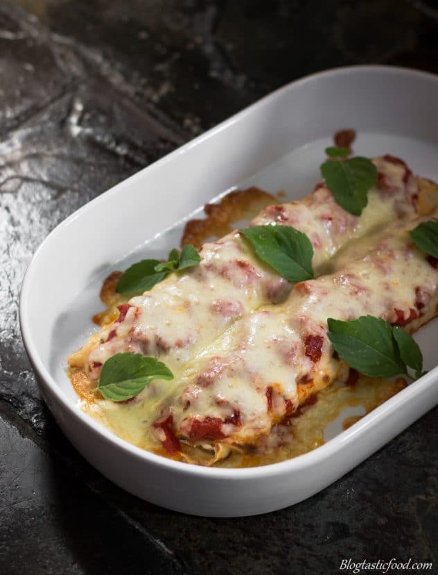 A photo of spinach and ricotta filled crepes that has been baked with tomato sauce and mozzarella cheese.