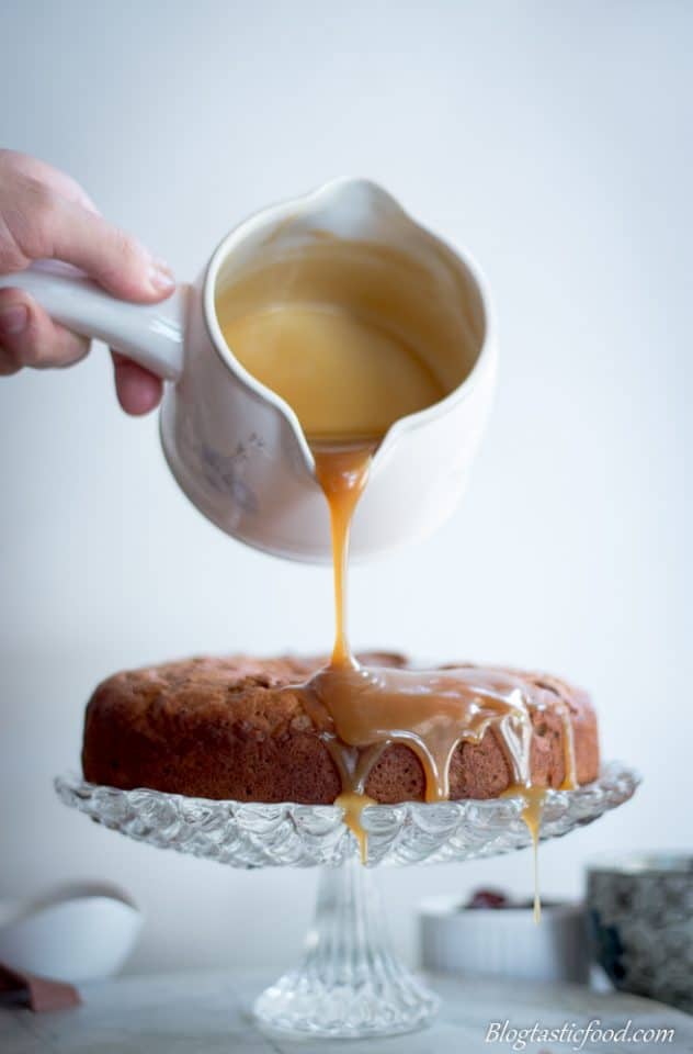 Someone pouring butterscotch sauce onto a sticky date pudding on a cake stand.