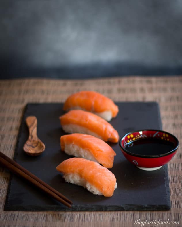 A platter of salmon sushi nigiri served with a mini bowl of say sauce.