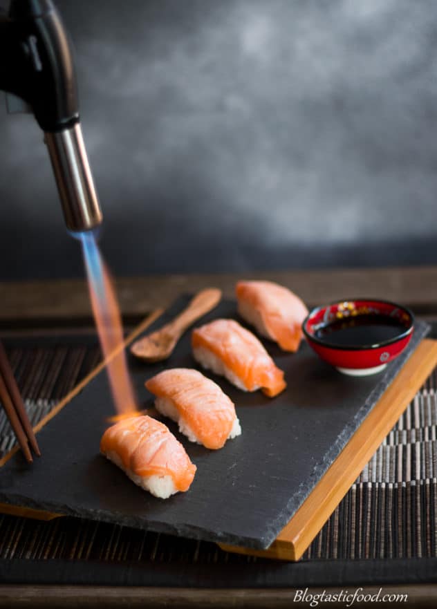 Someone using a blowtorch to sear fresh salmon sushi nigiri on a platter.