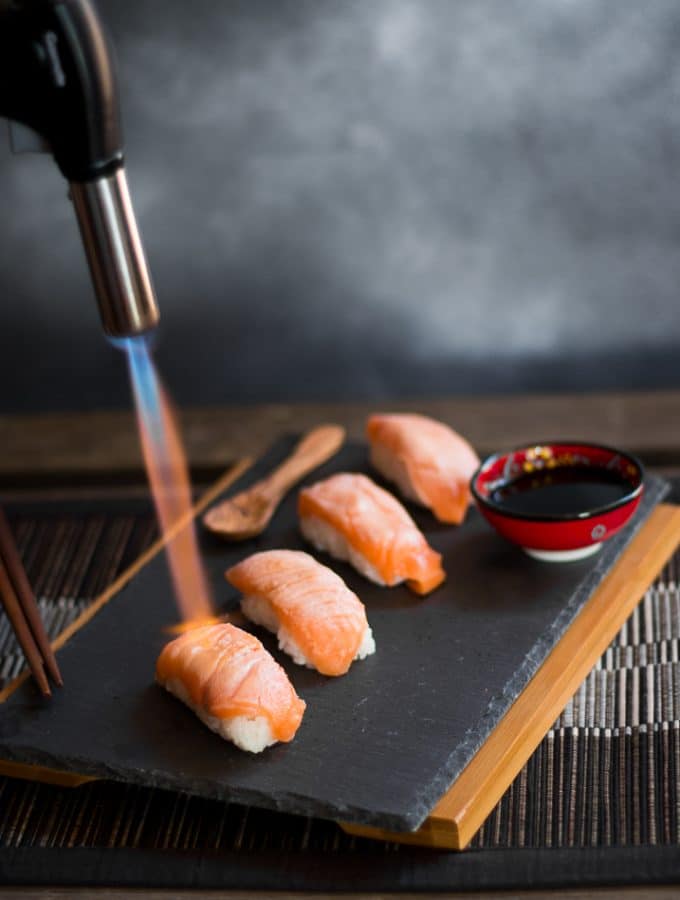 Someone using a blowtorch to sear the salmon on the sushi nigiri.