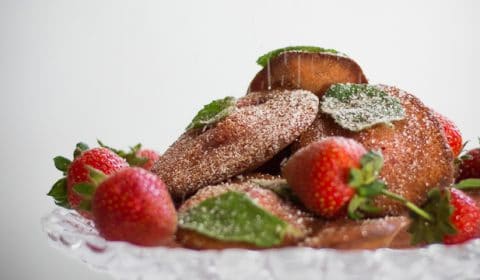 Strawberry madeleines and strawberries being dusted with icing sugar.