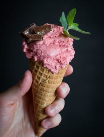 Someone holding a cone of strawberry ice-cream with a few flakes in it.