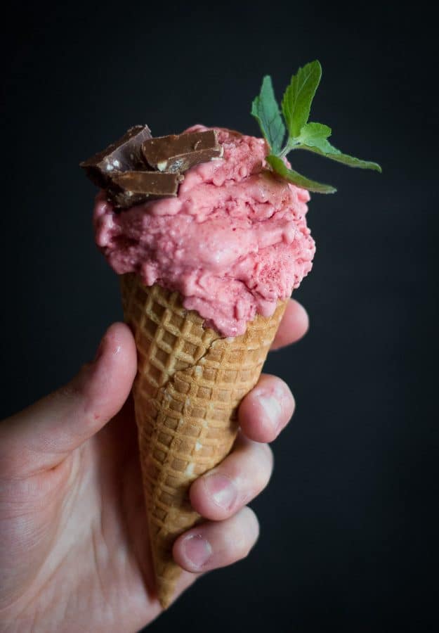 Someone holding a cone of strawberry ice-cream with a few flakes in it.