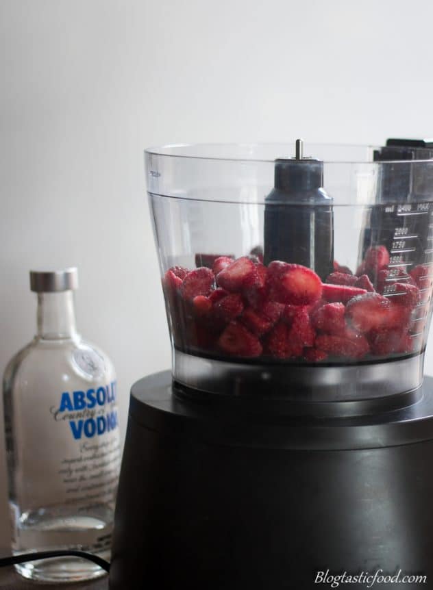 Frozen berries ready to be blended in a food processor. There is also a bottle of vodka in the background. 
