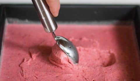 Someone using an ice-cream scoop to scoop out some strawberry and vodka ice-cream out of a tin.