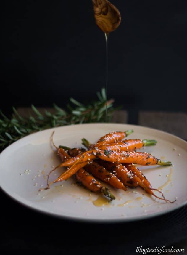 Someone drizzling honey over baby glazed carrots. 