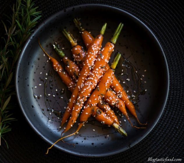 An overhead photo of baby glazed carrots in a black bowl. 