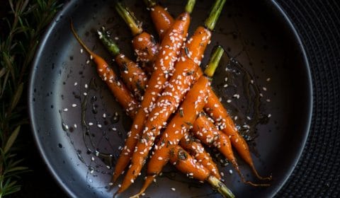 A photo of honey and butter glazed baby carrots garnished with sesame seeds.