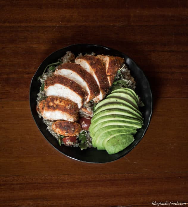 Sliced Cajun chicken and avocado over quinoa salad served on a black plate. 