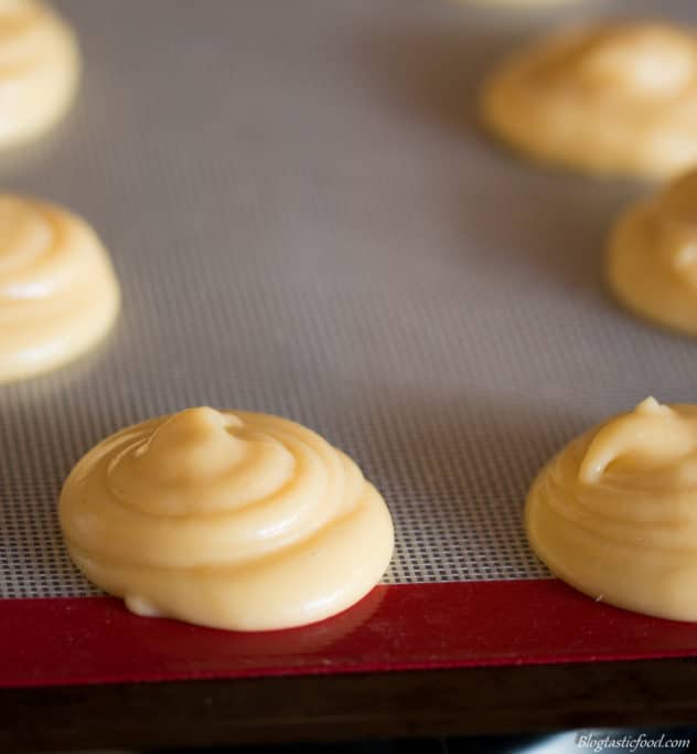 Choux pastry that has been piped in little blobs on a silicon mat. 